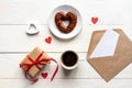 Valentines day mockup. Coffee, heart shaped chocolate cookie, gift box and paper card with craft envelope on white wooden table Royalty Free Stock Photo