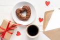 Valentines day mockup. Coffee, heart shaped chocolate cookie, gift box and paper card with craft envelope on white wooden table Royalty Free Stock Photo