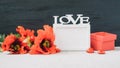 Valentines Day mockup with white frame with word LOVE, red poppies flowers and gift box on fabric and black background. Valentine