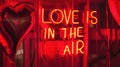 Valentines Day Neon vibrant red sign with phrase LOVE IS IN THE AIR and hearts