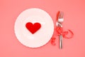 Valentine`s Day red heart on a white plate with fork and knife on pink background Royalty Free Stock Photo