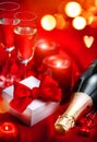 Valentines Day romantic dinner. Champagne, candles and gift box over holiday red background