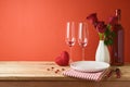 Valentines day romantic dinner concept. Wooden table with plate, wine bottle and rose flowers over red background Royalty Free Stock Photo