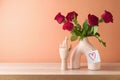 Valentines day romantic still life with red rose bouquet in modern vase on wooden table over peach color background Royalty Free Stock Photo