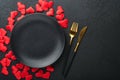Valentines day romantic table setting. Empty or closeup of a dinner black plate, knife, fork and decorative silk hearts on black b