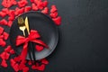 Valentines day romantic table setting. Empty or closeup of a dinner black plate, knife, fork and decorative silk hearts on black b