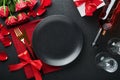 Valentines day romantic table setting. Empty closeup of red roses, wine, candles, dinner black plate, knife, fork and decorative Royalty Free Stock Photo