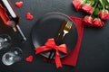 Valentines day romantic table setting. Empty closeup of red roses, wine, candles, dinner black plate, knife, fork and decorative Royalty Free Stock Photo