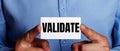 VALIDATE is written on a white business card in a man`s hands. Business concept