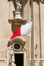 Valletta, Malta, August 2019. Maltese flag on the background of the facade of the Catholic Cathedral.