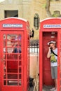 Valletta, Malta, July 2016. A cheerful boy is talking on the phone in a typical English telephone booth.