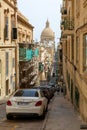 Typical Valletta street architecture with traditional Maltese rising road, wooden enclosed balconies and a dome of Basilica of Our