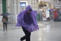 Person wearing purple emergency rain poncho running to hide from the falling rain, in Valletta, Malta