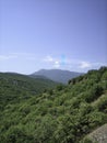 Valley of hills covered with low green forest. In the distance, the silhouettes of high mountains turn blue. Clear blue sky with Royalty Free Stock Photo