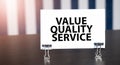 value quality service sign on paper on dark desk in sunlight. Blue and white background Royalty Free Stock Photo