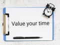 Value your time written on paper clipboard with alarm clock. Time management concept.