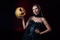 Vampire girl with fangs in black gothic dress holding Halloween pumpkin on black background Royalty Free Stock Photo