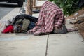 A homeless person huddles under a blanket on the sidewalk