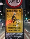 Vandalized street sign for cyclist that reads cross at green light in the middle of a city highway