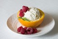 Vanilla Icecream with raspberry, summer dessert. Delicious sundae scoop in an orange half on a white plate Royalty Free Stock Photo
