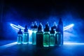 Vape concept. Smoke clouds and vape liquid bottles on dark background. Light effects.