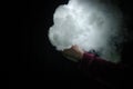 Vaping man holding a mod. A cloud of vapor. Black background. Vaping an electronic cigarette with a lot of smoke