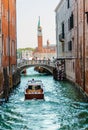 vaporetto amongst tall buildings cruising a venetian canal to the gran canal with a bridge plenty of tourists at the back and