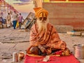 An Indian sadhu sits cross-legged, collecting donations.