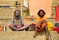 Varanasi, India: Two hindu bearded sadhu, pilgrim with damru on spear sitting in Hindu kesari orange