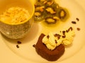 A variation of desserts served on a white plate: Chestnut chocolate terrine, marinated kiwi, and a vegan frangipane.