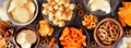 Table scene of various salty snacks, overhead view on a dark wood banner background Royalty Free Stock Photo
