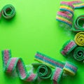 Rainbow stripes of sour jelly candies in sugar sprinkles on a green background with a place to copy.