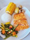 A varied, balanced lunch, rice, salmon steak, corn, and steamed vegetables