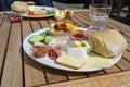 Varied breakfast or lunch plate in a street restaurant with sausage and ham, bread rolls, cheese and fruits on a wooden outdoor