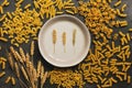 Varied pasta, ears of wheat, a plate on a dark background. Top view, flat lay