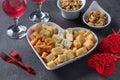 Varieties of elite cheese in a heart-shaped plate, cashews, peanuts and two glasses of wine for Valentine's Day on dark