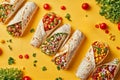 A variety of burritos with different fillings and vegetables scattered around on a yellow background