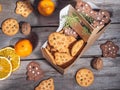 A variety of cookies in a paper bag, orange chips and tangerines lie on a wooden table