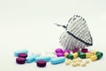 A variety of different coloured pills strewn around a white beaded wire heart. Set against a near-white background and surface. Royalty Free Stock Photo