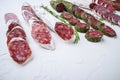 Variety of dry cured fuet and chorizosalami sausages, whole and sliced on white surface