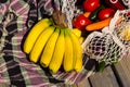Variety of fresh organic fruits and vegetables in avoska on the tablecloth. Banana, carrot, tomato in string bag. Healthy eating