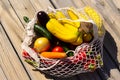 Variety of fresh organic fruits and vegetables in avoska on wooden surface. Banana, carrot, eggplant, tomato, cucumber and onion