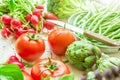 Variety of Fresh Organic Vegetables Artichokes Green Beans Tomatoes Red Radish Broccoli on Wood Garden Kitchen Table in Sunlight Royalty Free Stock Photo