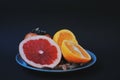 Variety of fruits on the blue plate. Grapefruit, oranges, persimmon and almonds on black background.