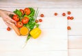 A variety of healthful vegetables - carrot, pepper, greens on a bright background. A hand holding a tasty tomato.