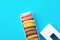 Variety of multicolored different flavors pink chocolate coffee yellow mocha macarons in white gift box with lid on mint blue