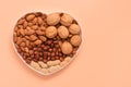 A variety of nuts in a bowl a heart shape on a pink pastel background. Almonds, walnuts, hazelnuts, peanuts. Top view, flat lay,