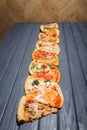 A variety of pizzas lie on a wooden table. Side view.