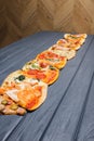 A variety of pizzas lie on a wooden table. Side view.