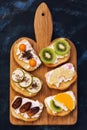 A variety of sweet sandwiches with fruit on a cutting board. Top view, blue background.